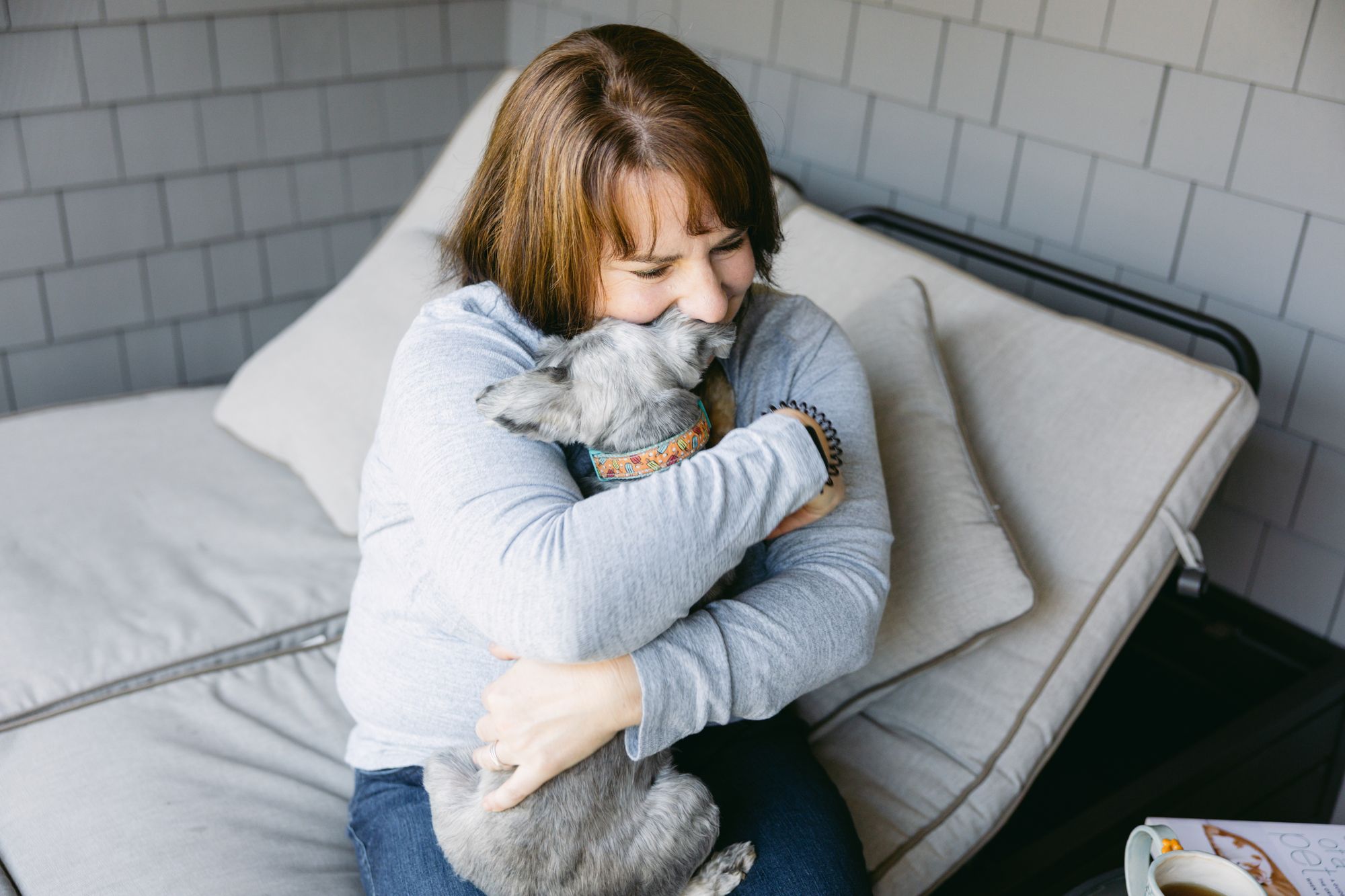 A woman hugging her grey schnauzer on a daybed